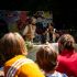 Kinder sitzen im Publikum und schauen einer Musikvorführung im Freien zu.